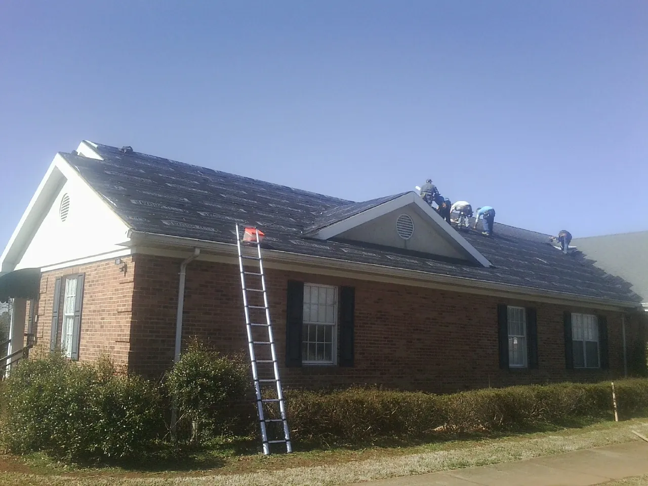 Crew tearing shingles off a brick ranch roof with a ladder set — Emergency Roof Repair work by our crew in New Palestine