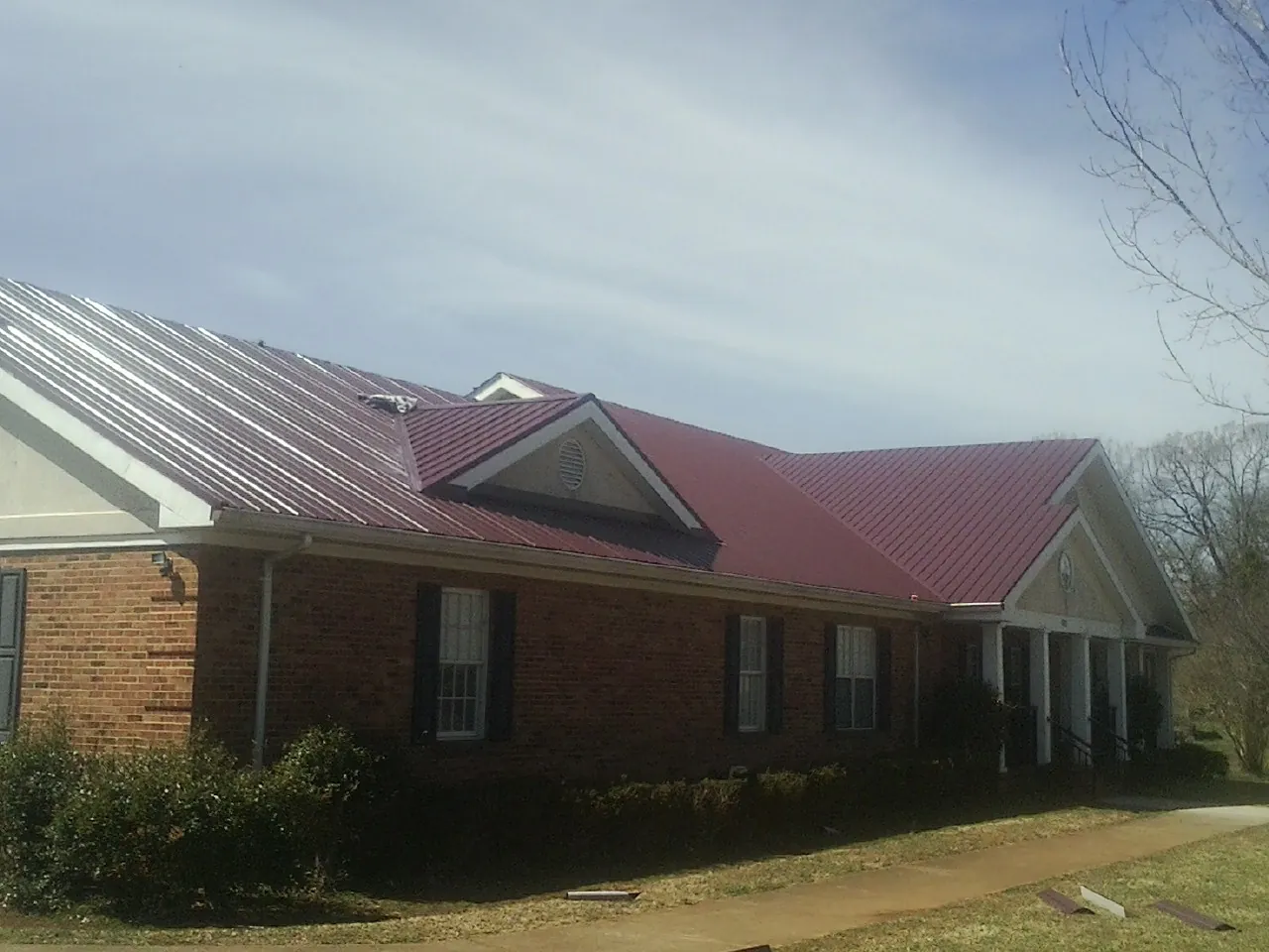 Red metal roof with gabled entries on a long brick building, from a Hail Damage Roof Repair job in New Palestine