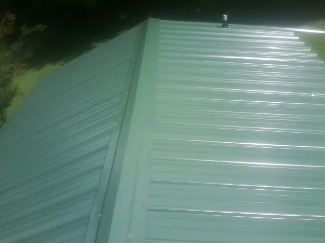 New green metal panels meeting at the ridge of a roof — Flat Roof Repair work by our crew in New Palestine
