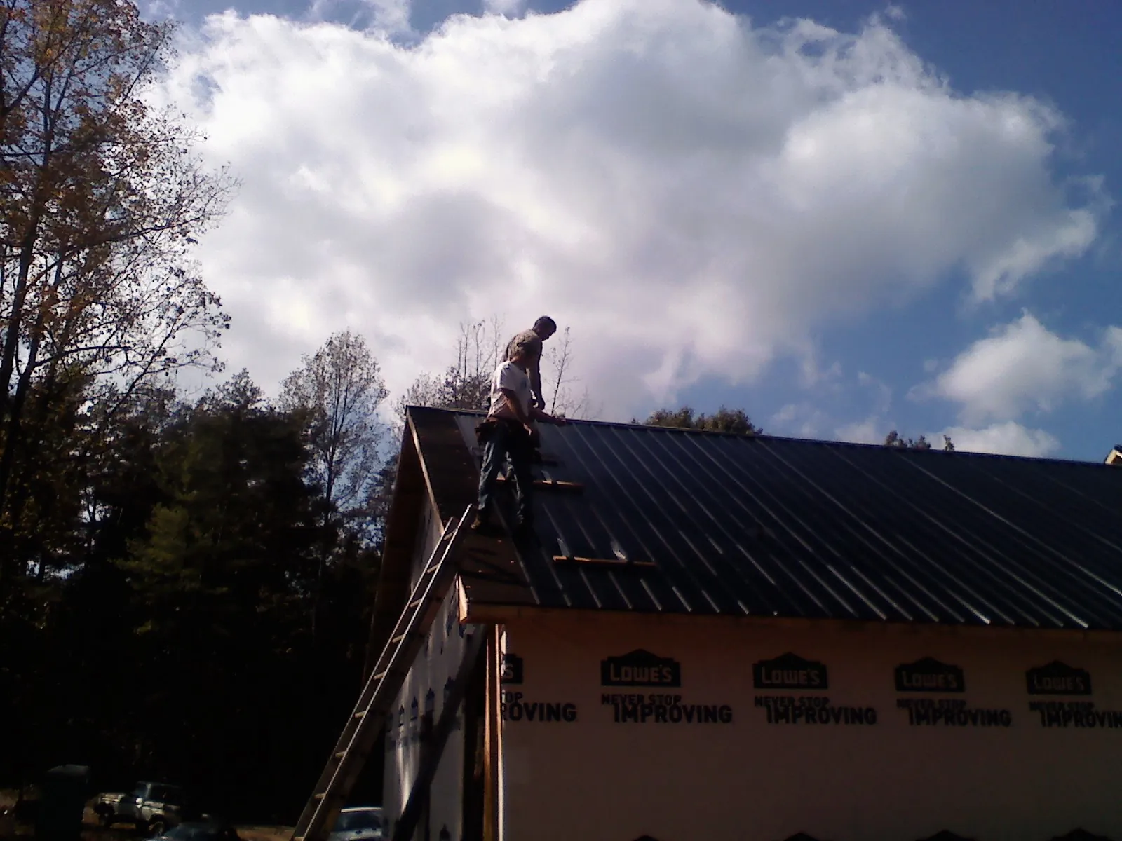 Roofer fastening dark metal panels high against a cloudy sky, from a Roof Inspection job in New Palestine