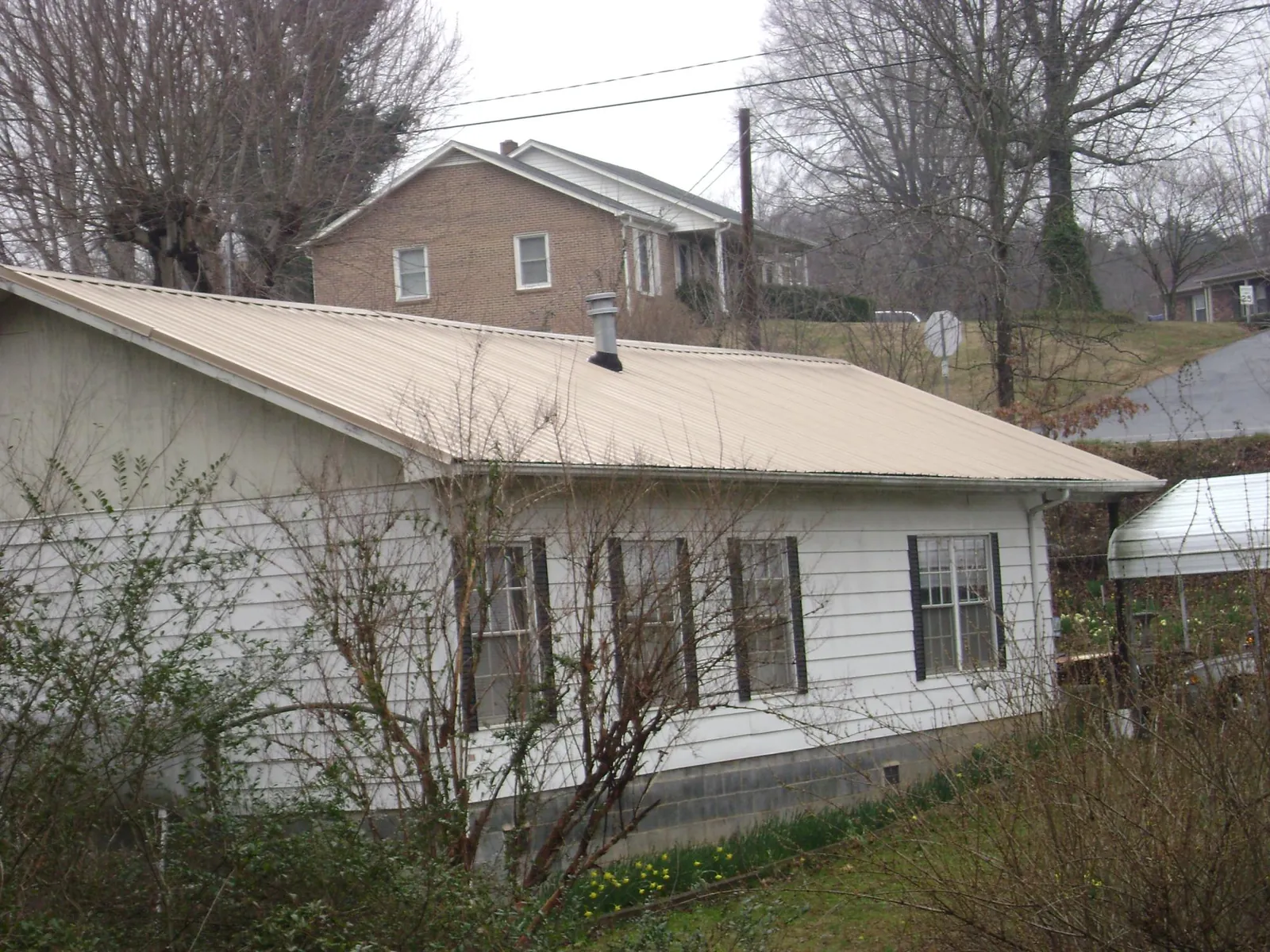 Tan metal roof on a white sided house set into a hillside — Commercial Roofing by Roofing Brothers in New Palestine