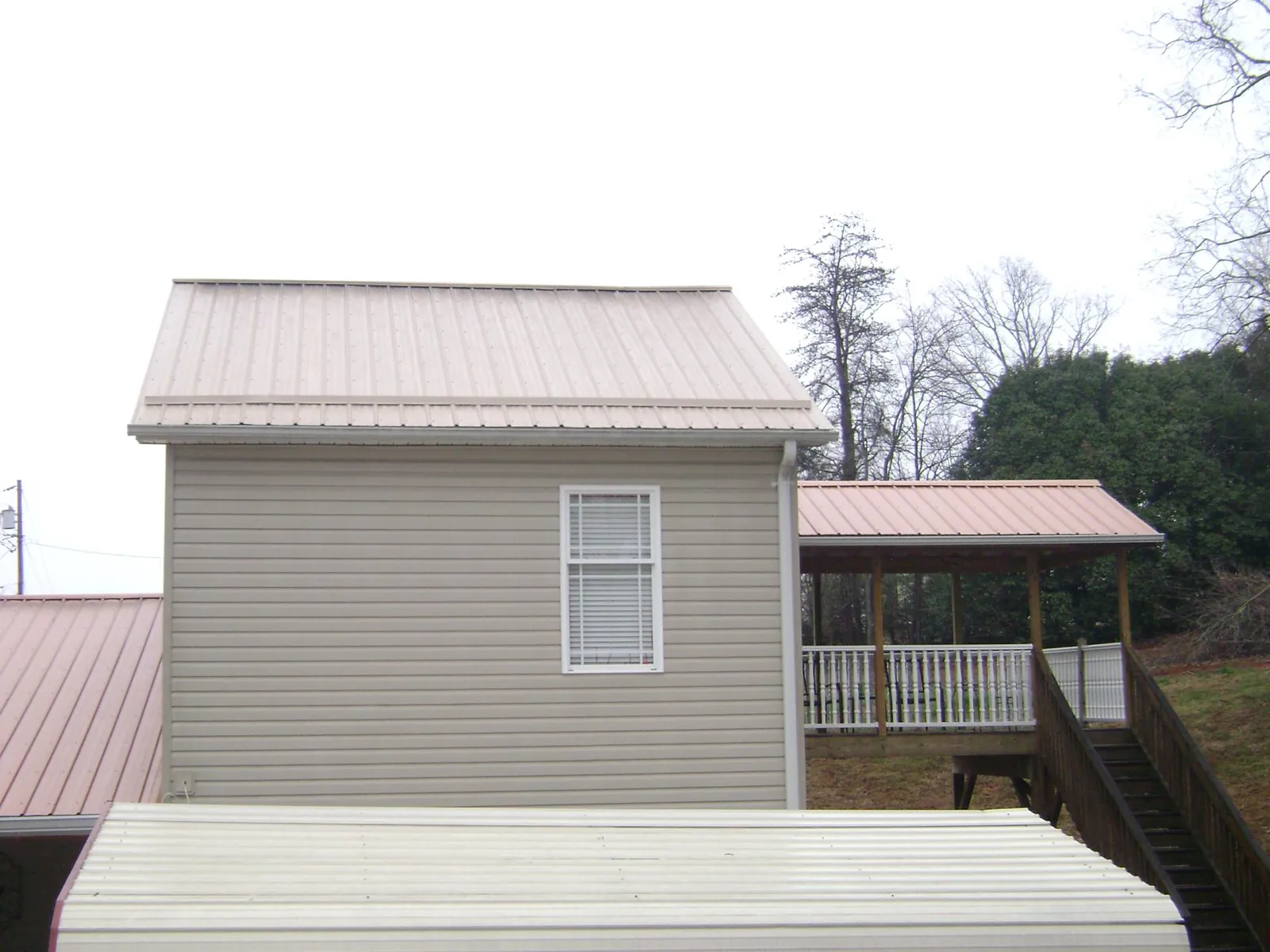 Tan metal roofs on a two story addition and attached porch, from a Roof Replacement job in New Palestine